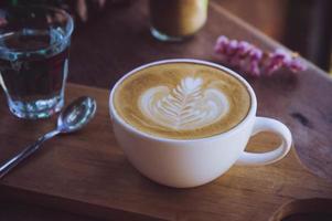 taza blanca de café con leche en la mesa de madera en la cafetería por la mañana foto