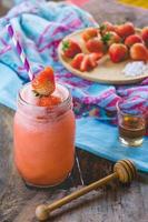jugo de batido de fresa, sobre miel sabrosa para el verano en la mesa de madera, jugo de agua dulce para la salud foto