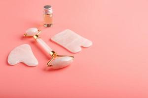 herramienta de masaje gua sha hecha de rodillo de cuarzo rosa natural, piedra de jade y aceite, sobre un fondo rosa para el cuidado de la cara y el cuerpo. parte de la medicina tradicional china foto