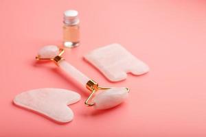herramienta de masaje gua sha hecha de rodillo de cuarzo rosa natural, piedra de jade y aceite, sobre un fondo rosa para el cuidado de la cara y el cuerpo. parte de la medicina tradicional china foto