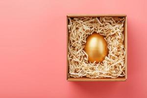 Golden egg in a box on a pink background. The concept of exclusivity, best choice, prize, special surprise, expensive gift. photo