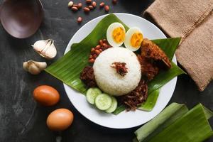 nasi lemak, es un malayo tradicional hecho con huevos cocidos, frijoles, anchoas, salsa de chile, pepino. del plato servido en una hoja de plátano foto