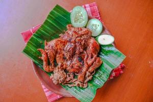 pollo a la parrilla o ayam bakar con pepino servido en hoja de plátano y plato. ayam bakar es pollo asado tradicional de indonesia foto