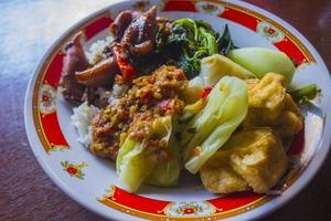 nasi tempong or sego tempong is traditional food from banyuwangi, indonesia made from rice, traditional fried squid, fried eggplant, cucumber slices, vegetables, spinach and spicy sambal  chili photo