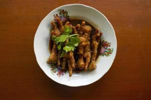 Spicy chicken feet with celery, chili, onion, garlic served with a white plate isolated from a black background. photo