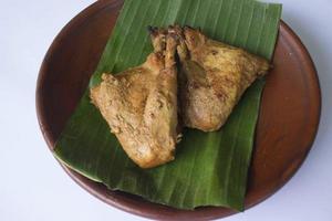pollo a la parrilla o ayam bakar o ayam panggang servido con hoja de plátano, cebolla en platos de barro, aislado de fondo blanco foto