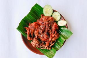 pollo a la parrilla o ayam bakar con pepino servido en hoja de plátano y plato. ayam bakar es pollo asado tradicional de indonesia foto