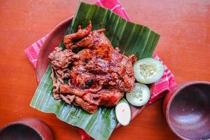 pollo a la parrilla o ayam bakar con pepino servido en hoja de plátano y plato. ayam bakar es pollo asado tradicional de indonesia foto