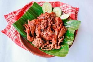 pollo a la parrilla o ayam bakar con pepino servido en hoja de plátano y plato. ayam bakar es pollo asado tradicional de indonesia foto