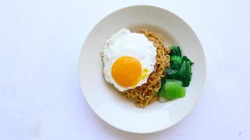 fideos instantáneos servidos con huevo frito y hojas de mostaza en un plato. indomie de fideos fritos instantáneos foto