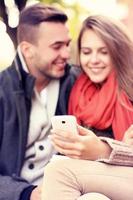 retrato borroso de una pareja joven en un banco con teléfono inteligente en el parque foto