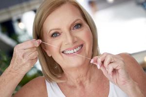 Senior woman using dental floss in the bathroom photo