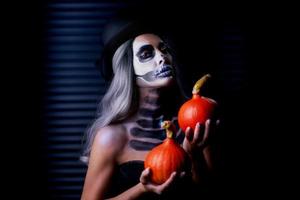 Spooky portrait of woman in halloween gotic makeup holding pumpkin photo