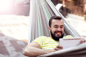 imagen que muestra a un hombre feliz descansando en una hamaca con una tableta foto