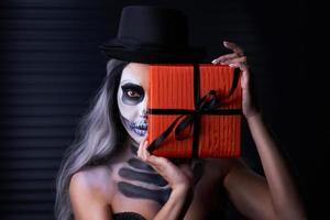 Spooky portrait of woman in halloween gotic makeup holding present photo