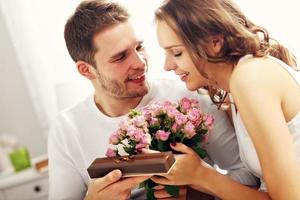 Man giving flowers and present to woman in bed photo