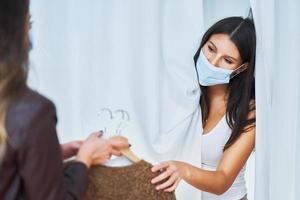 Two girl friends in clothes store in changing room in mask photo