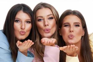 Three women in pastel suits posing over white background photo