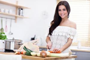 mujer joven tratando de preparar sopa de pollo en la cocina foto