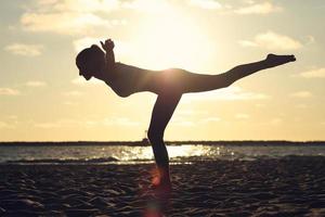 silueta, mujer joven, practicar, yoga, en la playa, en, ocaso foto