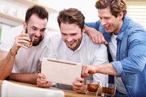 Cheerful friends having fun with smartphone and drinking at home photo