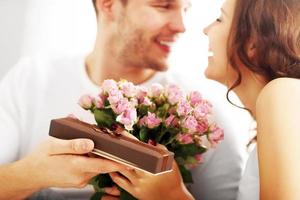 hombre dando flores y regalo a la mujer en la cama foto