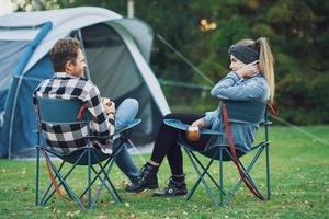 Una pareja joven y agradable sentada en sillas frente a la carpa en el campamento foto