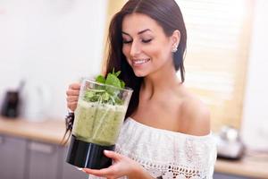 Fit smiling young woman preparing healthy smoothie in modern kitchen photo