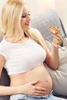 Beautiful pregnant young woman eating cake at home photo