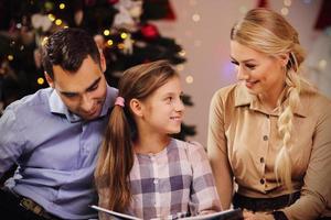 Family reading story book together under Christmas tree photo