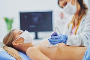 Doctor in mask checking up breast to her patient photo