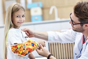 Male pediatrician checking bandage of little girl's broken arm photo