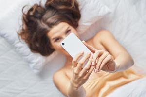 Happyadult woman using smartphone in bedroom in the morning photo