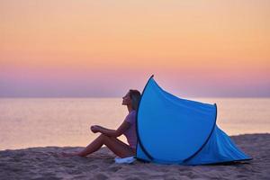 Silhouette of young woman in front of a tent at the beach at sunrise photo