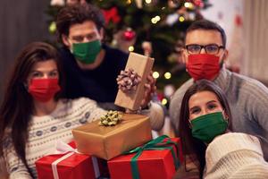 Group of friends wearing masks exchanging Christmas presents at home photo