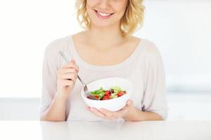 mujer joven comiendo ensalada en la cocina foto