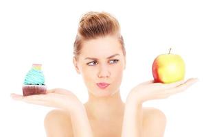 Woman trying to make a decision between cupcake and apple photo