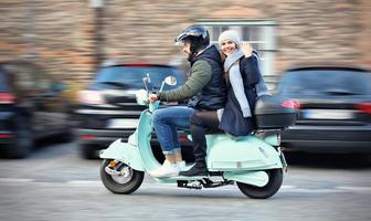 hermosa pareja joven sonriendo mientras monta scooter en la ciudad en otoño foto