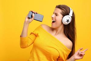 Beautiful woman listening to music on smartphone over yellow background photo