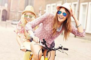 Two happy girl friends riding tandem bicycle photo