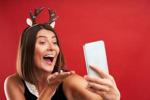 Adult happy woman in Christmas mood taking selfie over red background photo