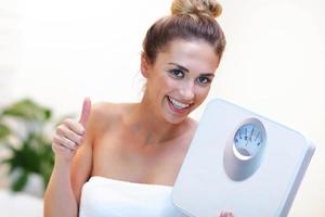 Happy woman holding bathroom scales in bathroom photo