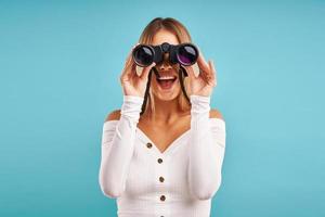 Beautiful adult woman posing over blue background with binoculars photo