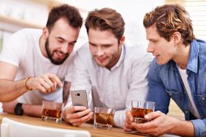 Cheerful friends having fun with smartphone and drinking at home photo