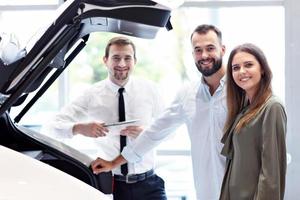 Confident young salesman explaining car features to the young attractive owners photo