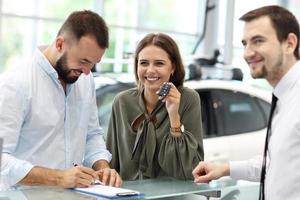 Confident young salesman explaining car features to the young attractive owners photo