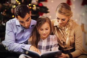 Family reading story book together under Christmas tree photo