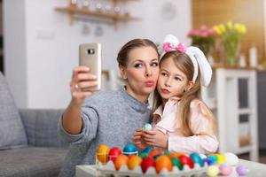 Mother and daughter painting Easter eggs and taking selfie photo