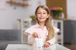 niña joven con alcancía sentado en la mesa foto