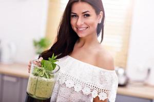 Fit smiling young woman preparing healthy smoothie in modern kitchen photo